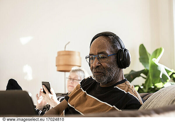 Senior man with headphones using laptop at home