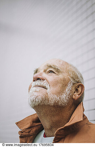 Senior man with looking up while standing against wall