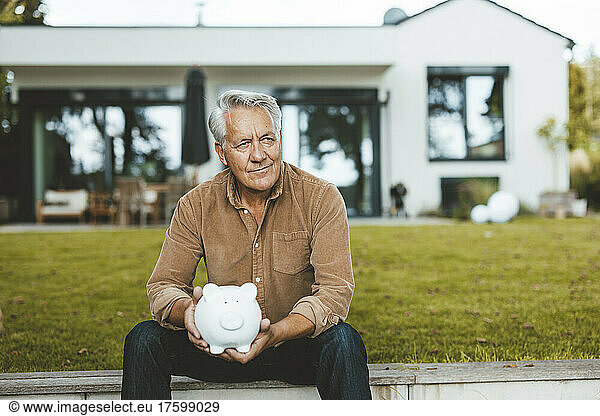 Senior man with piggy bank sitting at backyard