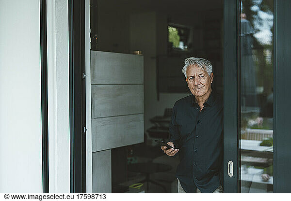 Senior man with smart phone standing at doorway