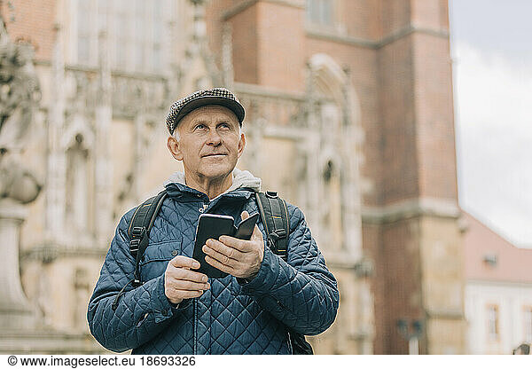 Senior man with smart phone standing in front of cathedral