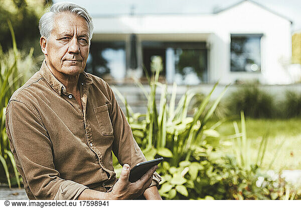 Senior man with tablet PC sitting at backyard
