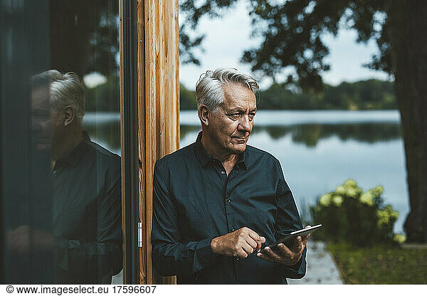 Senior man with tablet PC standing by glass wall at backyard