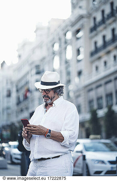 Senior man with white clothing and hat using smart phone in street of Madrid