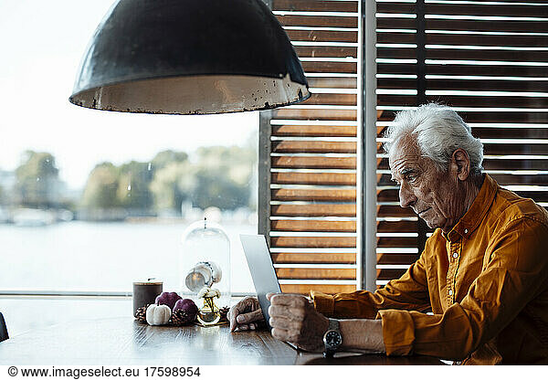 Senior man with white hair using laptop sitting at table in houseboat