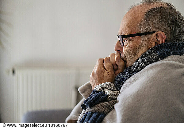 Senior man wrapped in blanket feeling cold at home