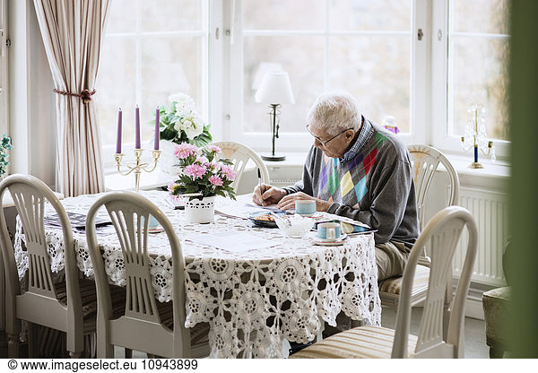 Senior man writing in book at dining table in nursing home