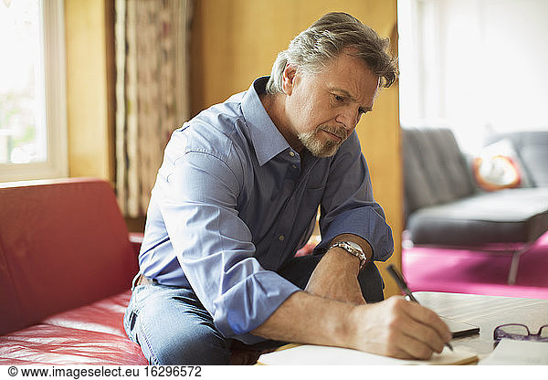Senior man writing in notebook at living room coffee table