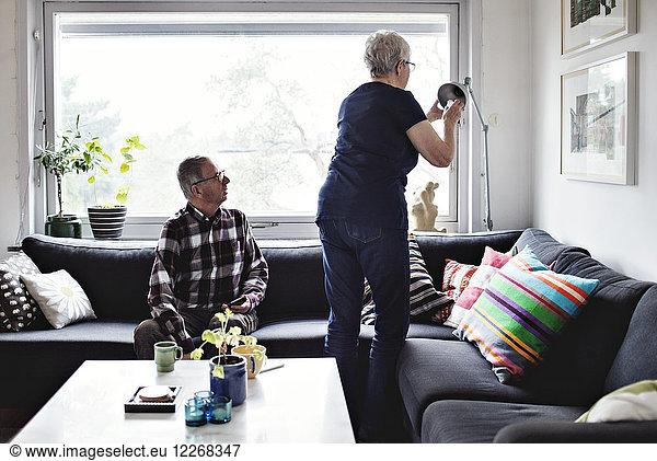 Senior Mann schaut auf die Frau  die die Stehleuchte am Sofa im Wohnzimmer verstellt.
