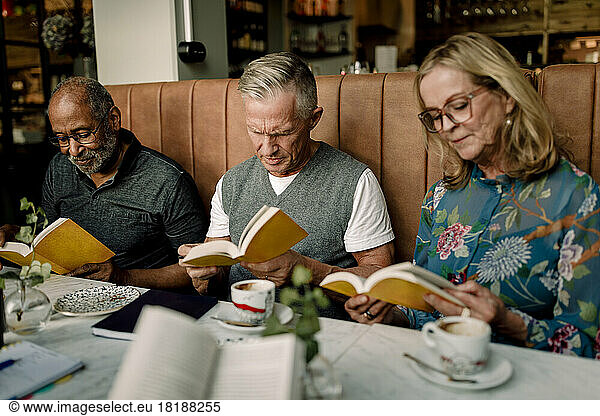 Senior men and woman reading books while sitting in cafe