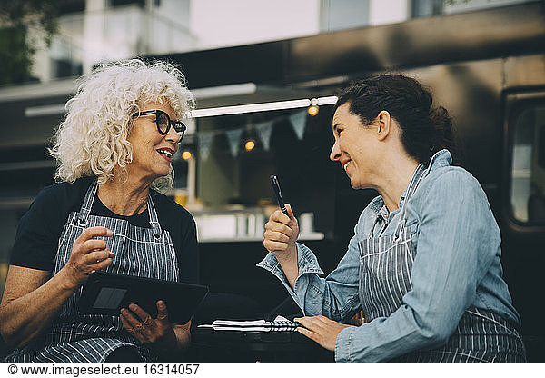 Senior owner talking to assistant against food truck in city