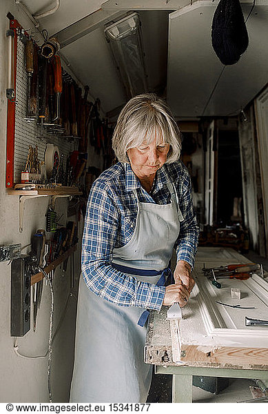 Senior-Unternehmerin kratzt in Ladenwerkstatt an Fensterrahmen