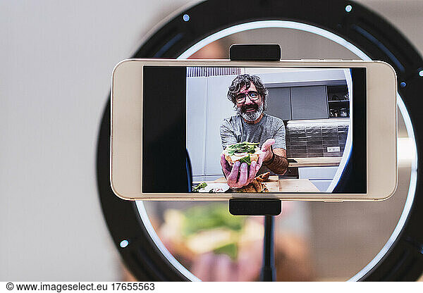 Senior vlogger presenting food through mobile phone at home