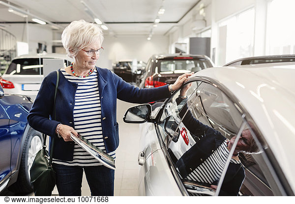 Senior woman admiring car in dealership store