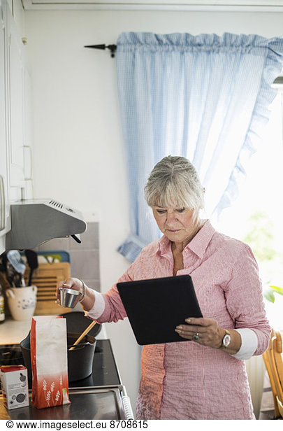 Senior woman cooking while looking at recipe on digital tablet