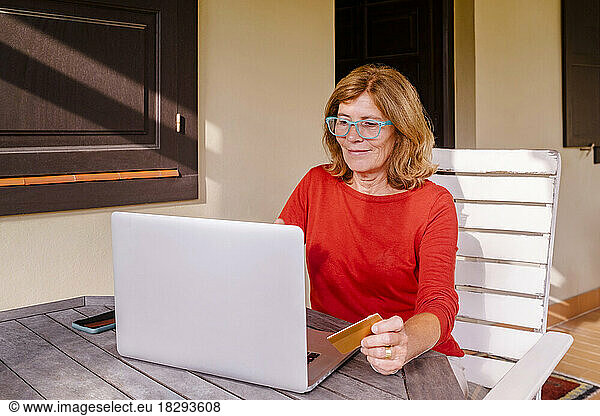 Senior woman doing online shopping with credit card and laptop at porch