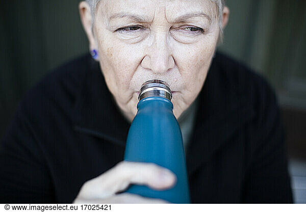 Senior woman drinking water outside house