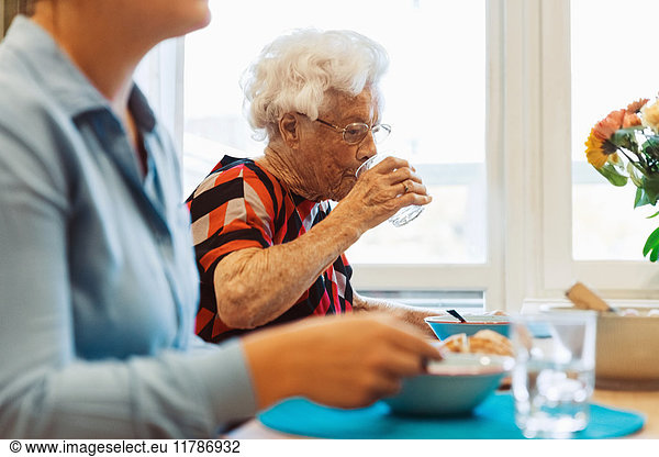 Senior woman drinking water while sitting with daughter at dining table