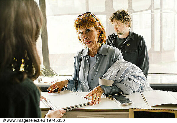 Senior woman giving damaged laptop to technician at repair shop