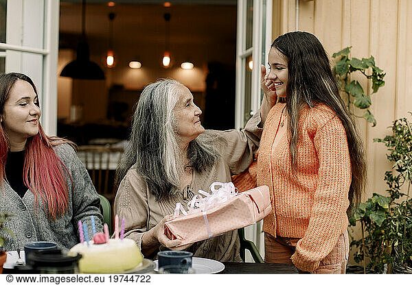 Senior woman holding birthday gift by granddaughter at patio