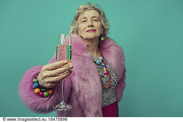 Senior woman holding champagne class against turquoise background