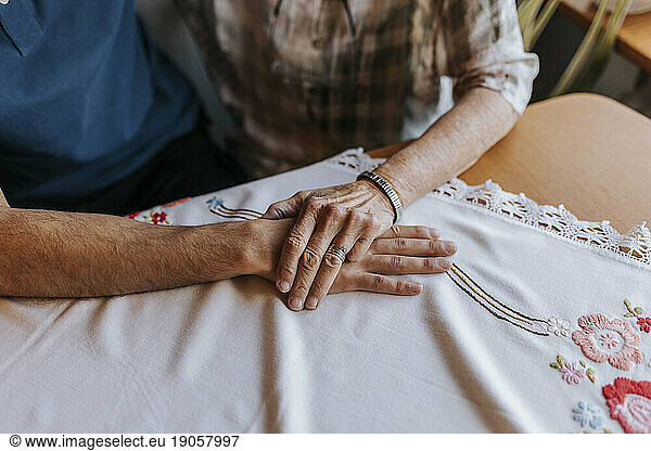 Senior woman holding hand of male caregiver over tablecloth at home