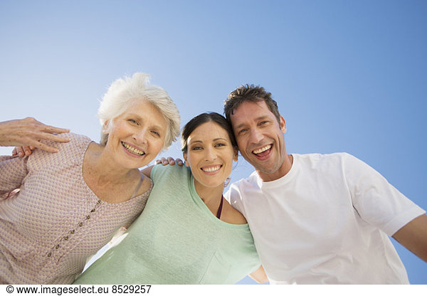 Senior woman hugging couple against blue sky