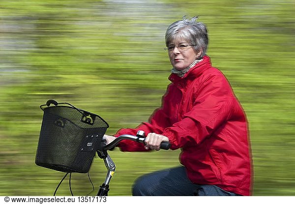 Senior woman in a red jacket riding a bike