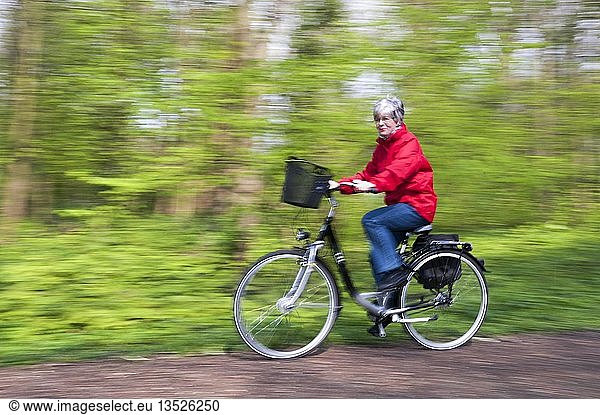 Senior woman in a red jacket riding a bike through the woods