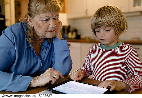 Senior woman looking at grandson using digital tablet