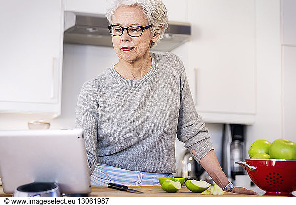 Senior woman looking at recipe on digital tablet while standing in kitchen