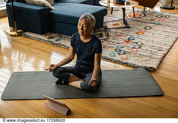 Senior woman meditating while learning through digital tablet at home