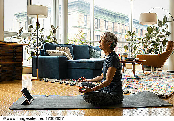 Senior woman meditating while learning through digital tablet in living room at home