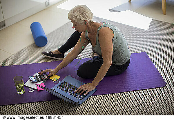 Senior woman paying bills and exercising at laptop on yoga mat