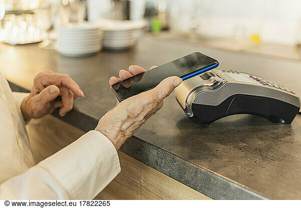Senior woman paying through mobile phone at cafe