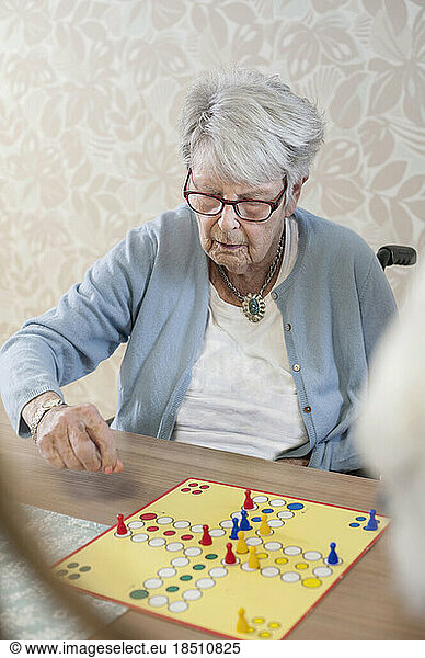 Senior woman playing ludo board game in rest home