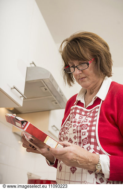 Senior woman reading ingredient box in kitchen