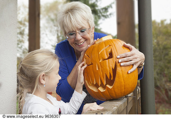 Senior woman showing Halloween pumpkin to her granddaughter