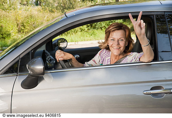 Senior woman sitting in car and showing victory sign