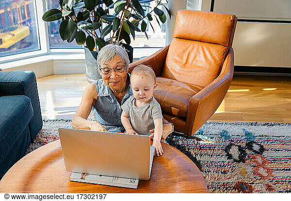 Senior woman sitting with granddaughter doing video call on laptop