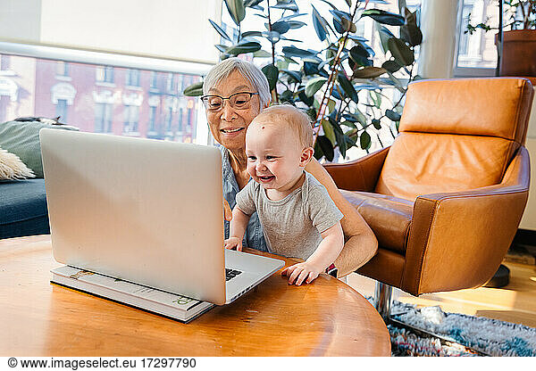 Senior woman sitting with granddaughter doing video call through lapto
