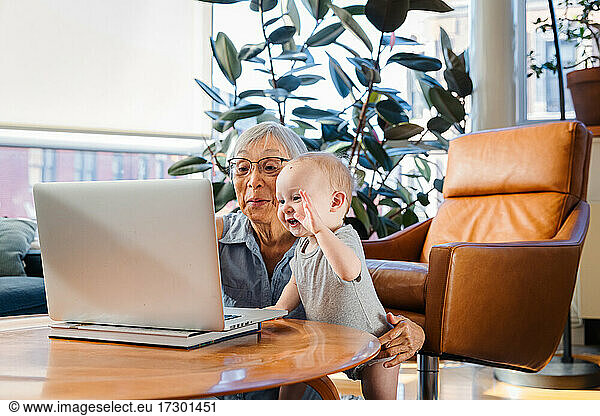 Senior woman sitting with granddaughter using laptop to video call