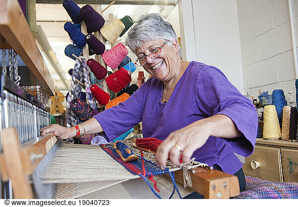 Senior woman smiling as she works on her loom at a fiber arts studio