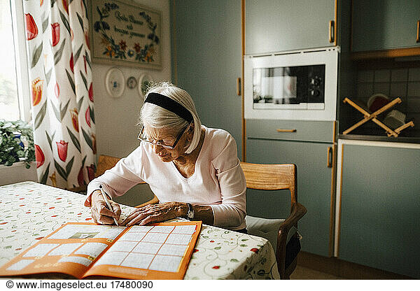 Senior woman solving sudoku at dining table in kitchen