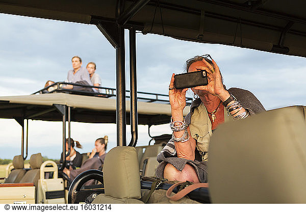 Senior woman taking picture with smart phone from a safari jeep.