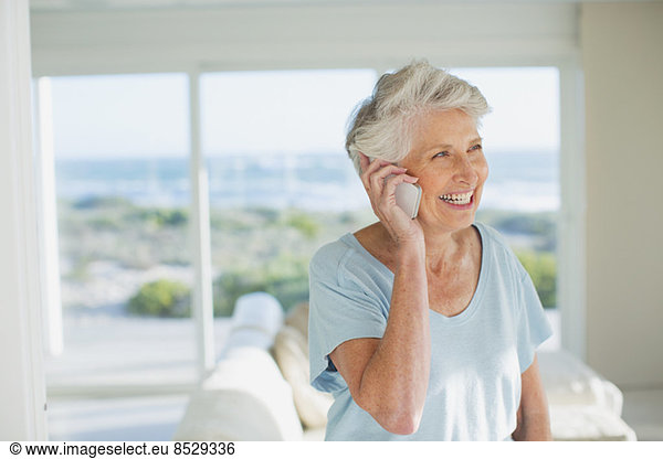 Senior woman talking on cell phone in sunny living room
