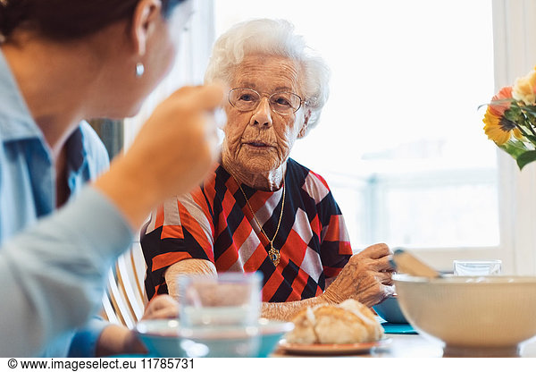 Senior woman talking to daughter while having food at home