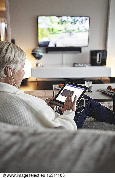 Senior woman using digital tablet while sitting on sofa in living room