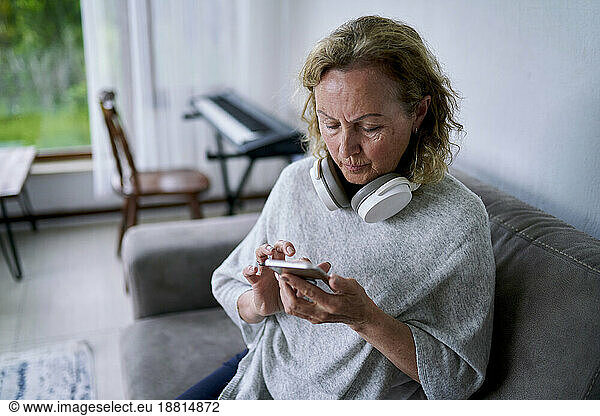 Senior woman using smart phone on sofa at home