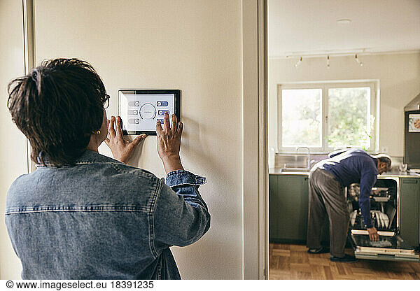 Senior woman wearing denim jacket using home automation on wall